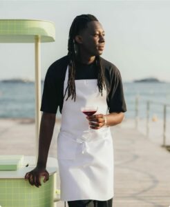 Mory Sacko, chef étoilé Michelin, posant en tablier blanc avec un verre à la main au bord de la mer.