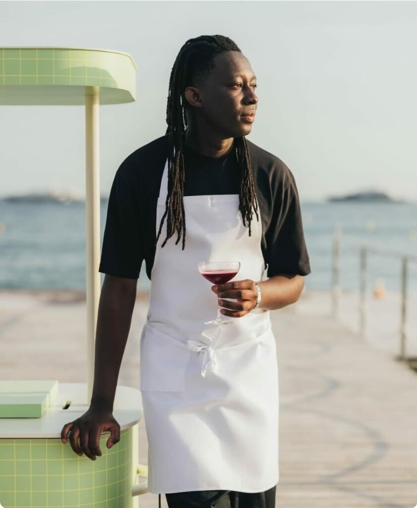 Mory Sacko, chef étoilé Michelin, posant en tablier blanc avec un verre à la main au bord de la mer.
